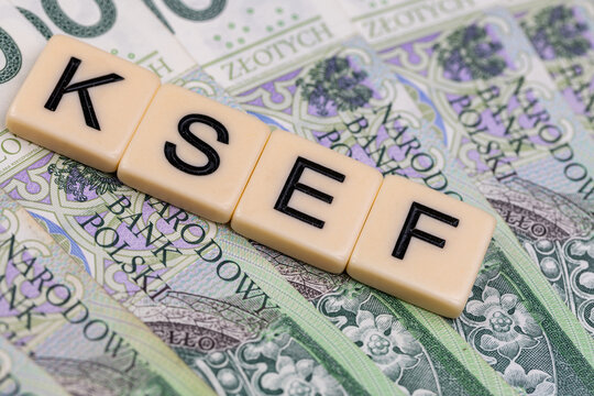 Blocks with the abbreviation KSEF, standing for National E-invoice System, are placed against a background of loosely spread Polish 100 PLN banknotes. The photo was taken under artificial lighting.