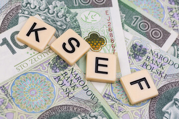Blocks with the abbreviation KSEF, standing for National E-invoice System, are placed against a background of loosely spread Polish 100 PLN banknotes. The photo was taken under artificial lighting.