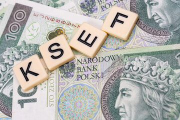 Blocks with the abbreviation KSEF, standing for National E-invoice System, are placed against a background of loosely spread Polish 100 PLN banknotes. The photo was taken under artificial lighting.
