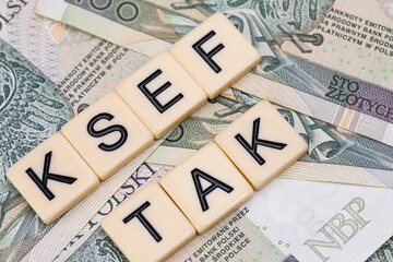 Blocks with the abbreviation TAK KSEF, standing for positives about National E-invoice System, are placed against a background of loosely spread Polish 100 PLN banknotes. 