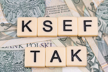 Blocks with the abbreviation TAK KSEF, standing for positives about National E-invoice System, are placed against a background of loosely spread Polish 100 PLN banknotes. 