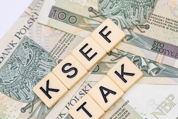 Blocks with the abbreviation TAK KSEF, standing for positives about National E-invoice System, are placed against a background of loosely spread Polish 100 PLN banknotes. 