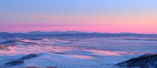 A snow-covered landscape under a pink and blue sky at sunset with distant mountains