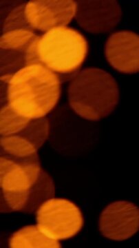 Warm orange bokeh lights on dark background softly drift and shimmer as camera defocuses and reframes, creating abstract holiday glow with gentle motion and copy space.