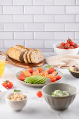 Healthy breakfast table with whole grain bread, smoked salmon, avocado and cherry tomatoes. Fresh ingredients on white tiled background. Clean eating and balanced lifestyle concept