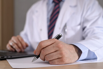 A doctor holding a pen, writing something on a piece of paper, writing out a prescription or referral
