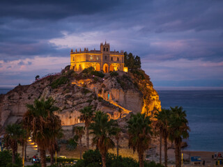 Tropea cliff sanctuary at dusk in Calabria, illuminated historic church on rocky promontory above Tyrrhenian Sea, dramatic clouds, coastal landmark, southern Italy travel destination