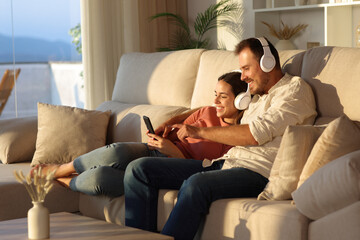 Happy couple wearing headphone sharing audio on phone