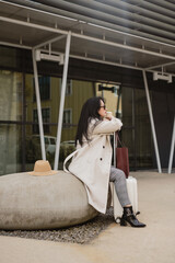 Woman waiting with luggage and coffee outside building