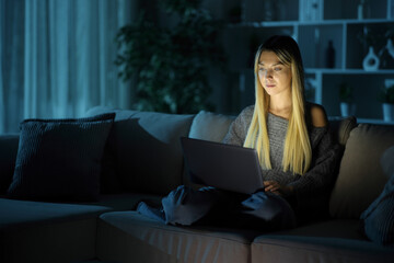 Serious woman using laptop sitting in the night at home