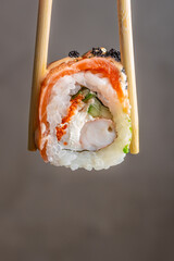 Sushi roll held with chopsticks close up isolated on neutral background