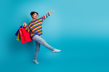 Obraz premium Young woman with colorful striped sweater joyfully shopping against blue background