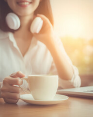 a happy woman in a white shirt with headphones, sitting at a desk and holding a coffee cup