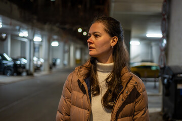 Fototapeta premium Portrait of woman standing outdoors at night in city street. Everyday urban lifestyle and thoughtful moment in real life environment