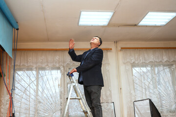 Man on Step Ladder Photo Studio Checking Ceiling Light Fixture.