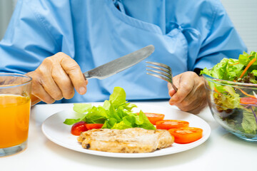Asian elderly woman patient eating salmon stake and vegetable salad for healthy food in hospital.