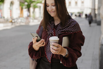 Woman on city street using phone with coffee