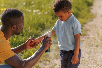 Dad carefully applies insect and tick protection to his little son, spraying repellent on his skin and clothing while spending time in nature © 24K-Production