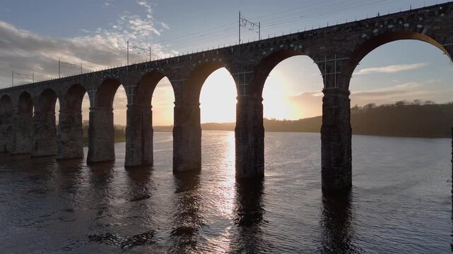 Aerial view of the Royal Border Bridge at sunset featuring the arches over the river with sun reflecting off the water, Berwick-upon-Tweed, England, United Kingdom.