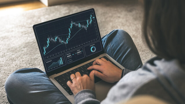 Trader Analyzing Live Financial Candlestick Charts and Investment Data on a Laptop Screen while Working Comfortably from Home - Powered by Adobe