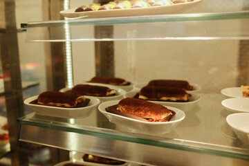 Tiramisu dessert portions served on white plates inside a cafe display case. Classic Italian dessert presentation for restaurant or pastry menu concept.