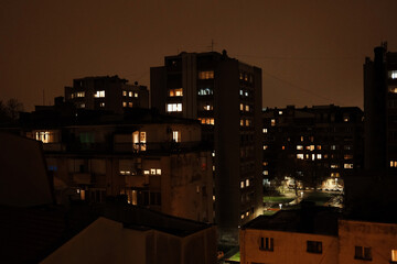Night view of residential apartment buildings with glowing windows under an overcast sky. Urban neighborhood atmosphere with warm city lights, quiet evening mood and dense housing skyline.
