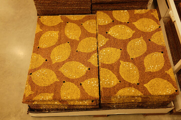 Stacked coir doormats with yellow lemon patterns displayed in a retail store, showing textured natural fibers and colorful graphic design.