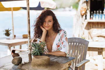 Stylish Woman In Deep V Dress Relaxing At Rustic Seaside Cafe Table