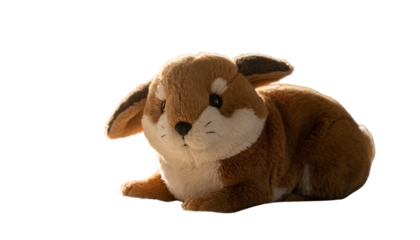 A small brown and cream colored stuffed animal fox with pointy ears is lying down on a white surface in the light