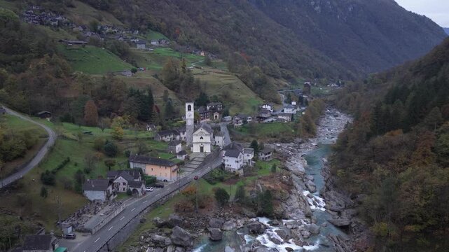 Aerial view of the white Lavertezzo Church beside a clear turquoise river flowing through the valley, a picturesque scene, Verzasca, Ticino, Switzerland.