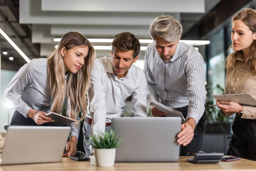 Business people discussing work together using a tablet and laptop taking notes in a modern office