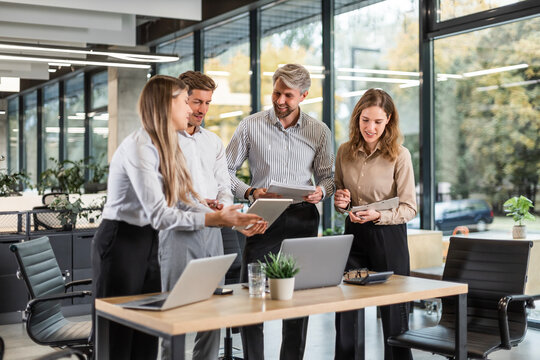 Group of business people standing together and discussing their work and projects, having a team meeting in an office.