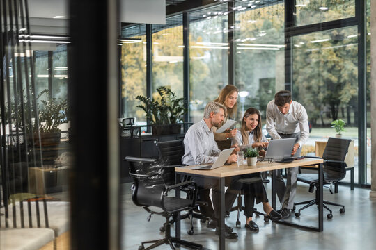 Group of business people standing together and discussing their work and projects, having a team meeting in an office, view from glass wall
