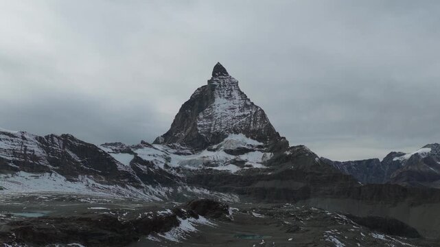 Aerial view of the imposing Matterhorn mountain, its snow-capped peak piercing the sky, amidst a landscape of rugged terrain and patchy snow cover, Zermatt, Valais, Switzerland.