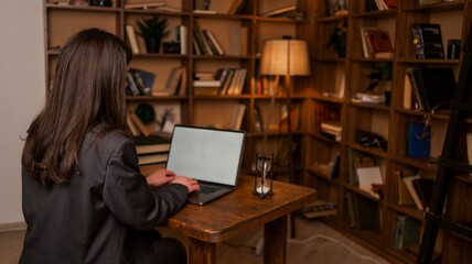 Woman in a suit typing on a laptop in a library with bookshelves and an hourglass © shine.graphics