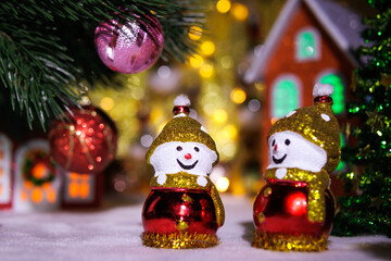 Two snowmen between Christmas trees against the backdrop of Christmas houses