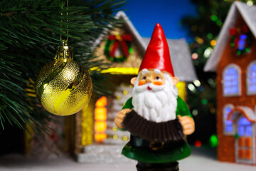 A gnome near a hanging Christmas ball on a Christmas tree branch against the backdrop of houses