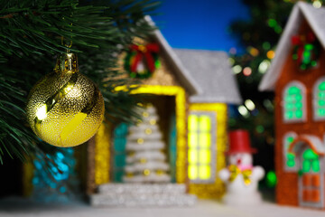 A Christmas ball hangs on a Christmas tree branch against the backdrop of houses