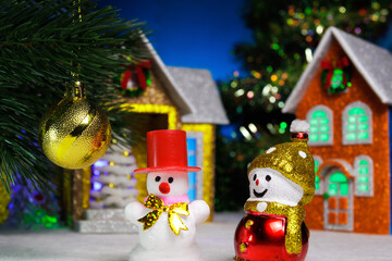 Two snowmen and a ball on a Christmas tree branch against the backdrop of houses