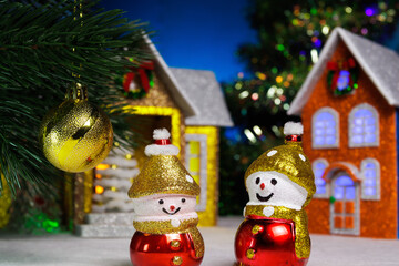 Snowmen and a ball on a Christmas tree branch against the backdrop of houses