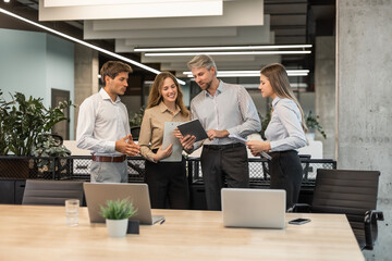 Group of business people standing together and discussing their work and projects, having a team meeting in an office.