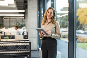 Young elegant business woman standing with digital tablet near office window