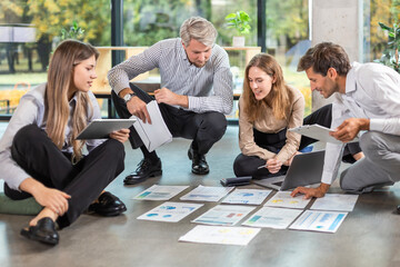 Group of young business people working on new project sitting with financial documents spread out on the floor