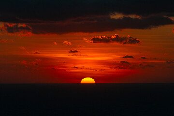 Malta sunset landscape. Dramatic sunset over the horizon of the Mediterranean Sea at Dingli Cliffs in Malta, with deep orange and red colors reflecting on the water under a dark cloudy sky. Sea sunset