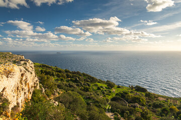 Naklejka premium Golden hour sunset at the rugged Dingli Cliffs in Malta, with warm light illuminating the rocky terrain and small clouds over the Mediterranean Sea.