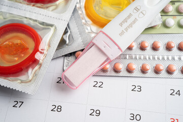 Pregnancy test and birth control pills on calendar, contraception health and medicine.