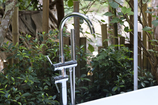 Modern chrome faucet sink tap with curved design standing outside near fresh green garden plants and nature background feeling clean peaceful and refreshing hygiene wash equipment for outdoors