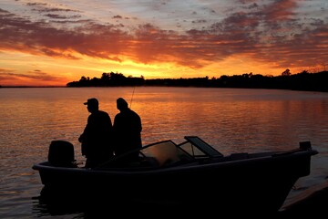 Dos pescadores en una lancha al amanecer con un cielo dramático de nubes rojas