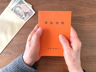 Senior holding pension booklet and cash on wooden table