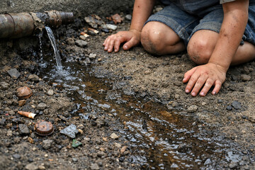 Person crouching beside a pipe leaking water onto dry ground with scattered debris